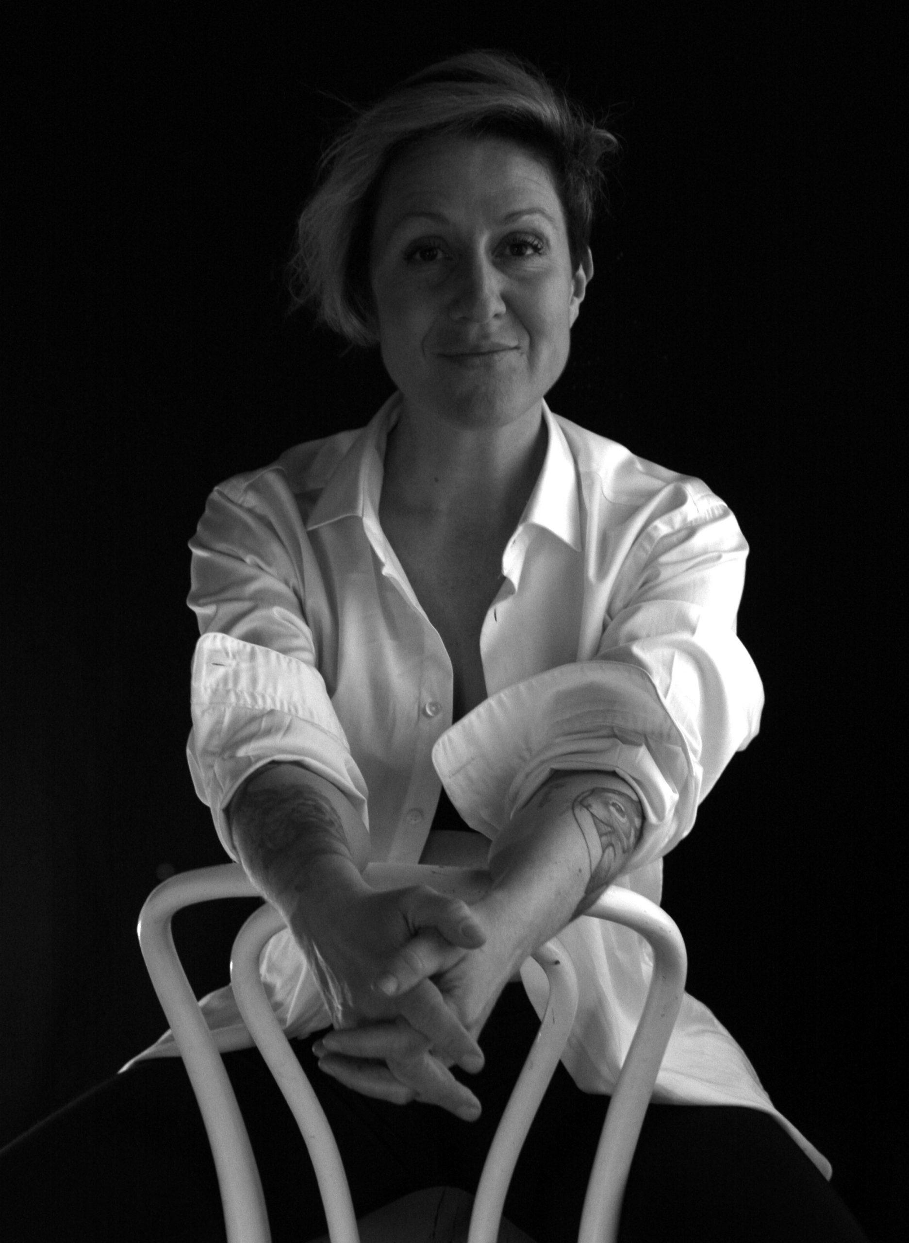 Black-and-white portrait of Essu Koskinen seated backward on a chair, wearing a white shirt.