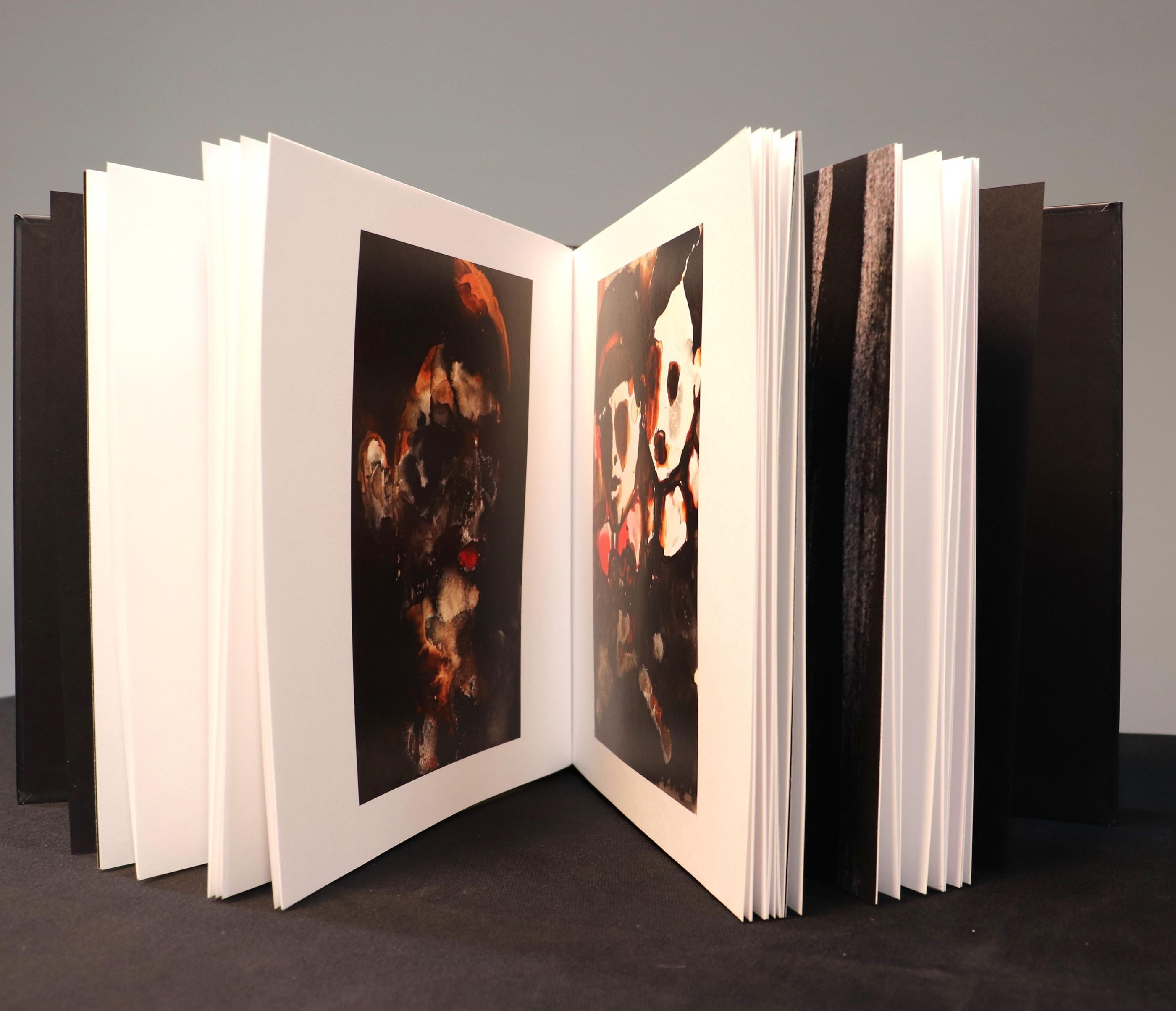 The artist’s book opened in a fan, revealing dark figurative paintings across its pages.