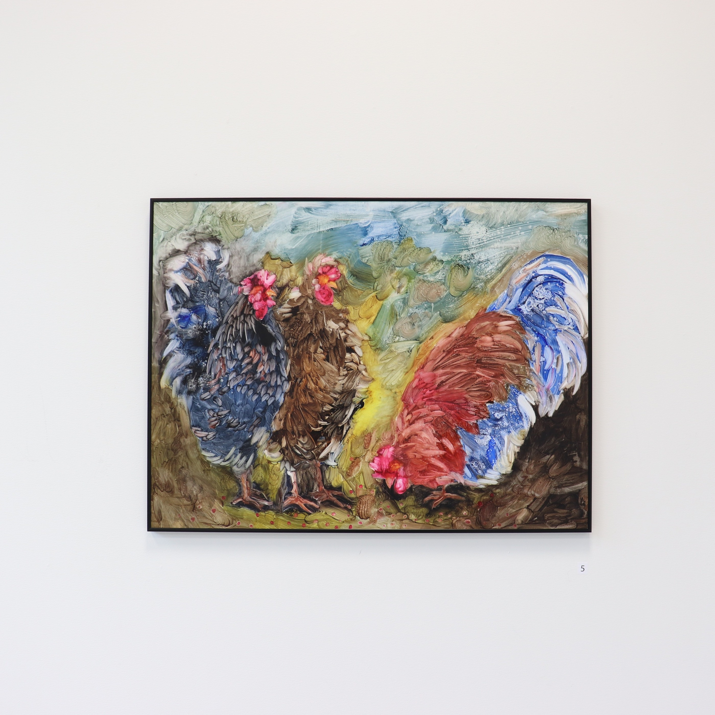A framed painting of three chickens in blue, brown, and red hung alone on a white gallery wall.