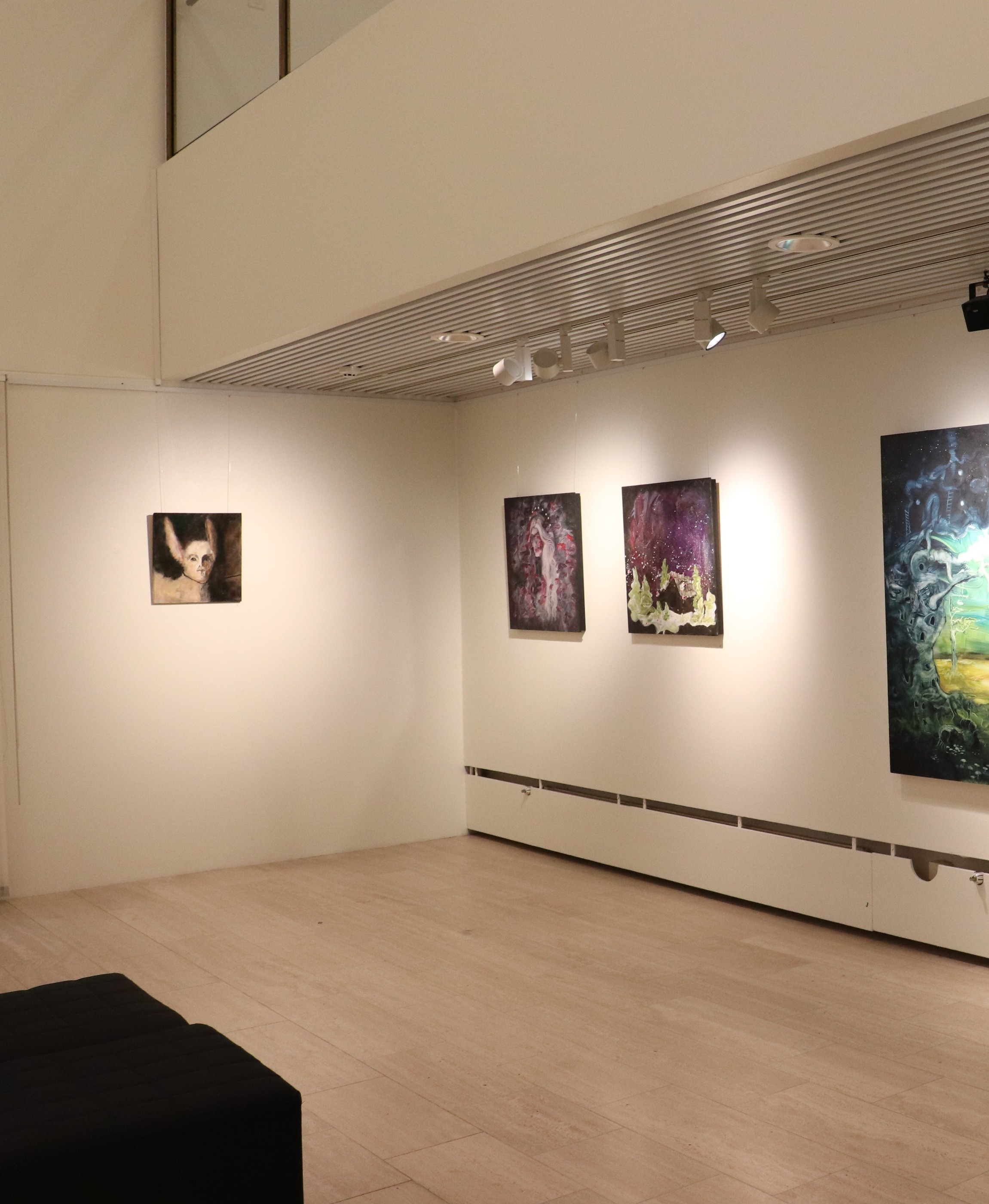 Valkoinen galleriatila, jonka kahdella seinällä on rivi tummia ja jalokivensävyisiä maalauksia.