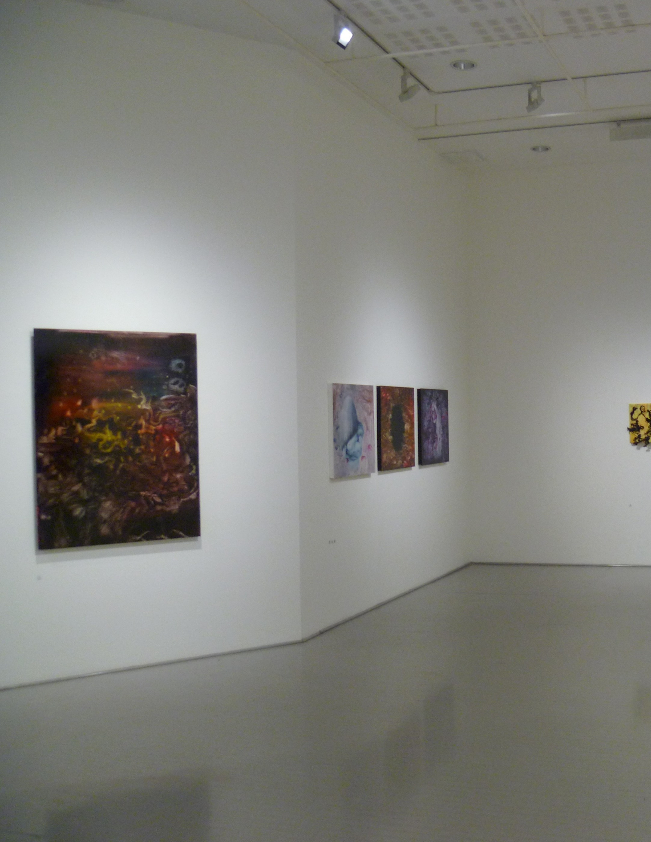 A spare white gallery with one dark painting in the foreground and smaller works beyond.